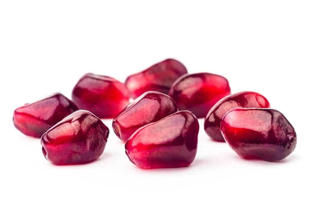Garnet fruit seeds with water drops isolated on white background. Group of pomegranate seeds closeup. Fresh garnet grains macro shot
