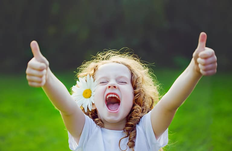Laughing girl with daisy in her hairs, showing thumbs up.