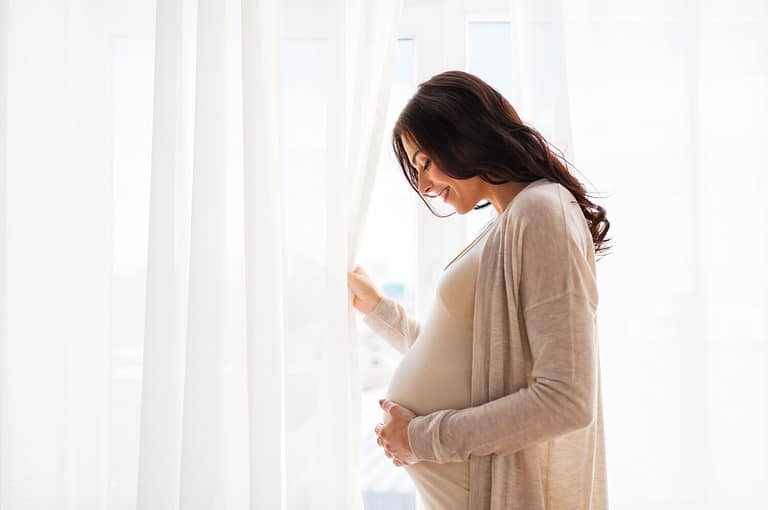 pregnancy, motherhood, people and expectation concept - close up of happy pregnant woman with big belly at window