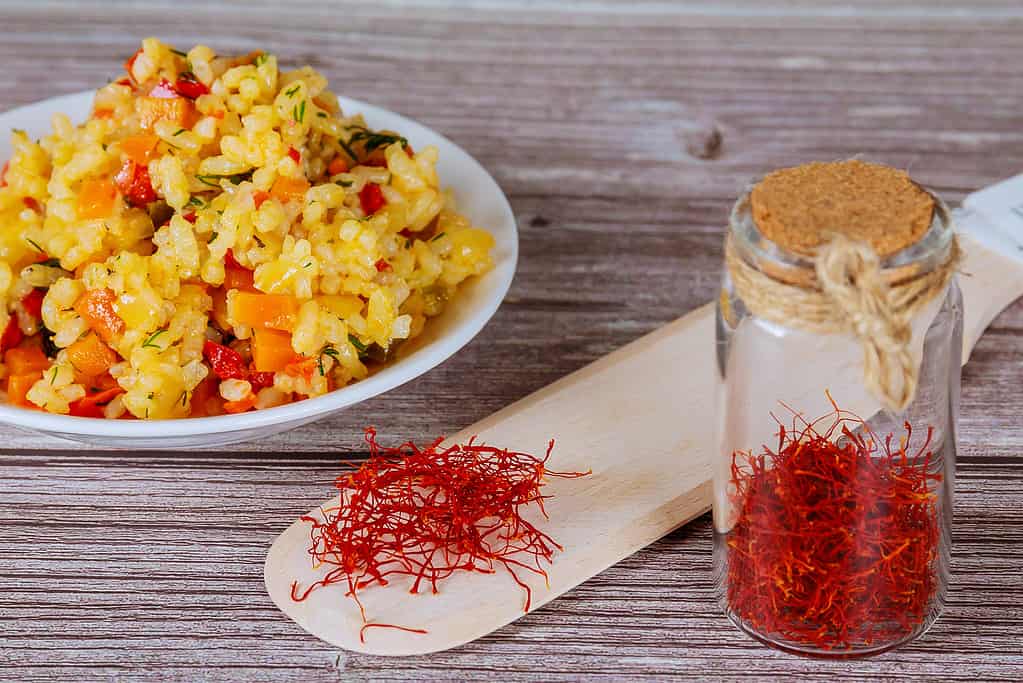 Rice with vegetables with saffron on a white plate on a wooden background.