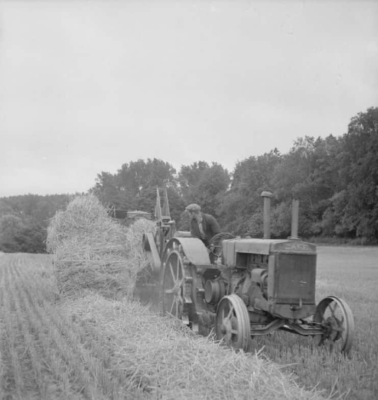 A 'pick-up baler' at work, circa 1943. The job of this machine is to follow behind the combine harvester and gather up the straw. This straw is then passed up a conveyor to a baling machine, which presses the straw into bales. One agricultural worker drives the vehicle, and two other men (not pictured) are needed to wire up the bales as they are produced.