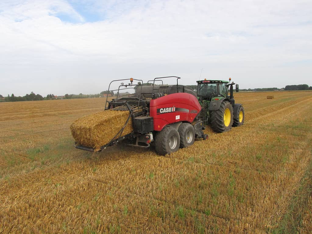 Hulst, Holland - aug 14, 2021: a tractor with a baler is putting a straw bale at the field