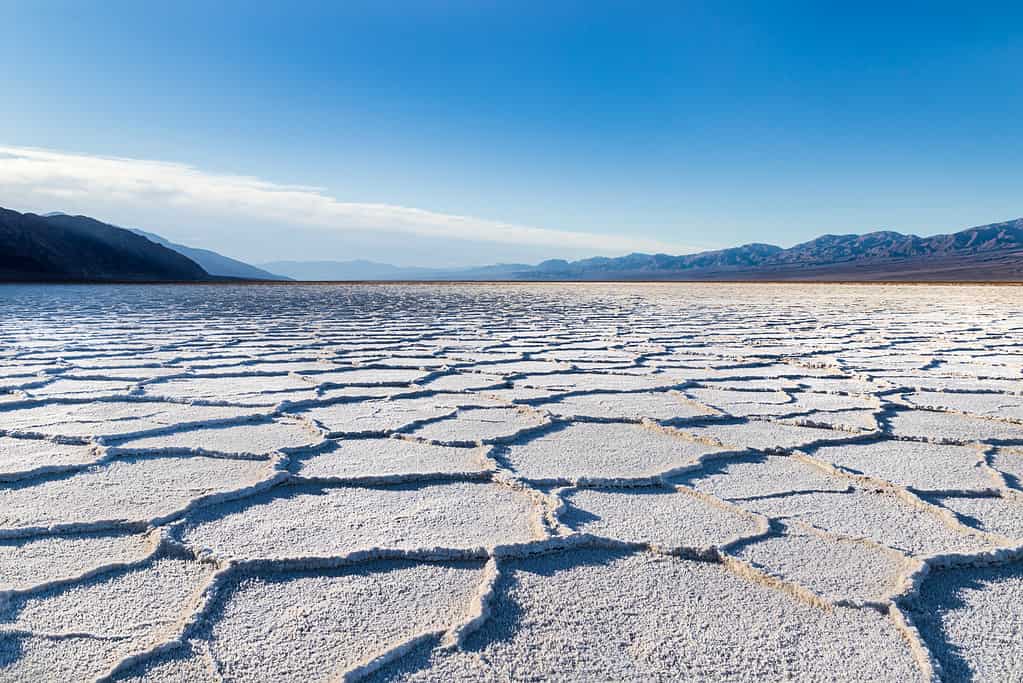 Sunrise over Badwater Basin, Death Valley, California. Sunburst over the far mountains; the basin floor is covered with white salt deposits; snaking crystal formations form hexagonal shapes into the distance.