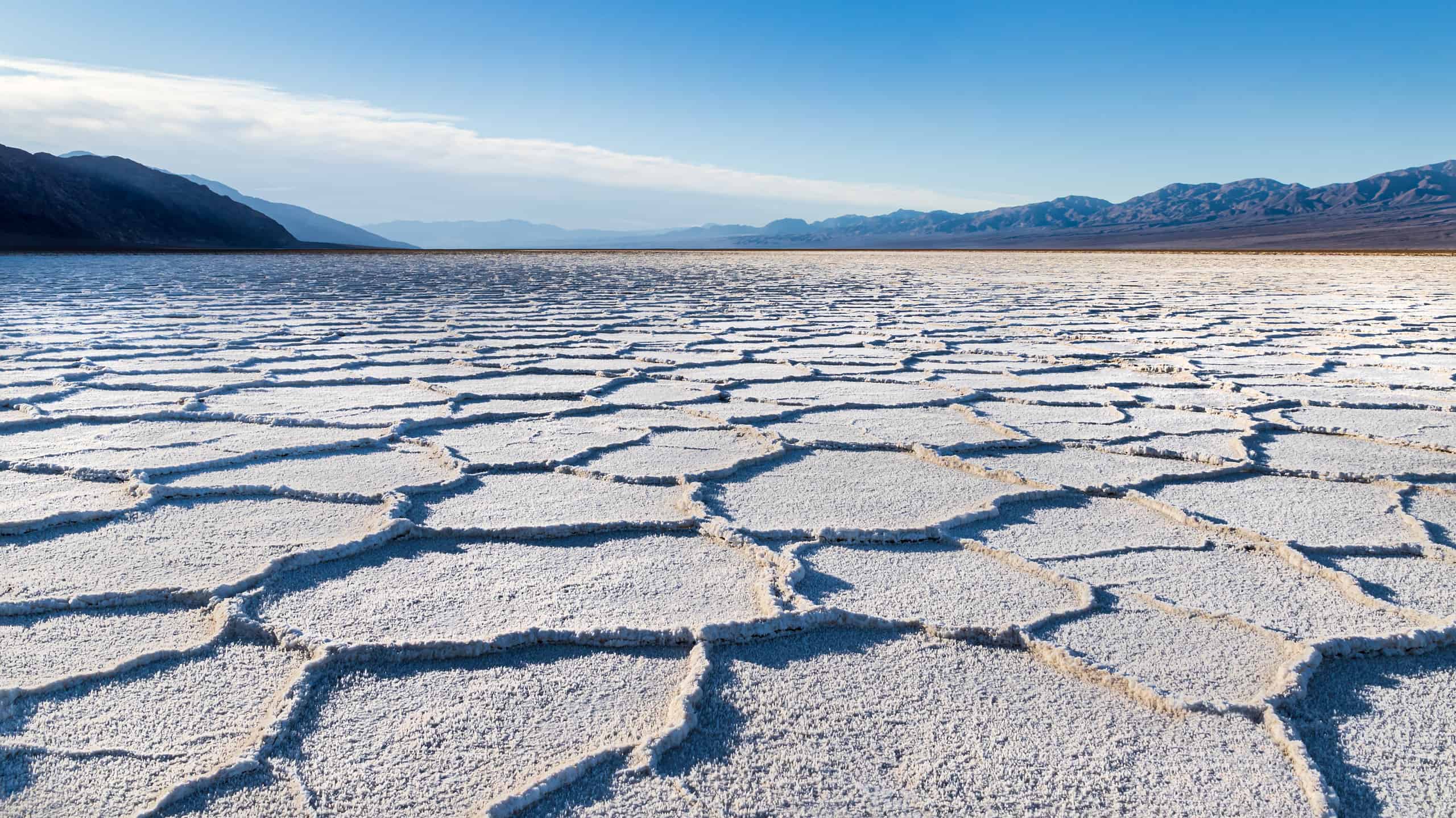 Sunrise over Badwater Basin, Death Valley, California. Sunburst over the far mountains; the basin floor is covered with white salt deposits; snaking crystal formations form hexagonal shapes into the distance.