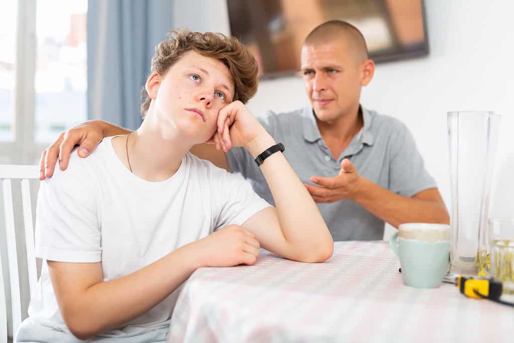 Teenager boy feeling upset. His father sitting next to him and comforting.