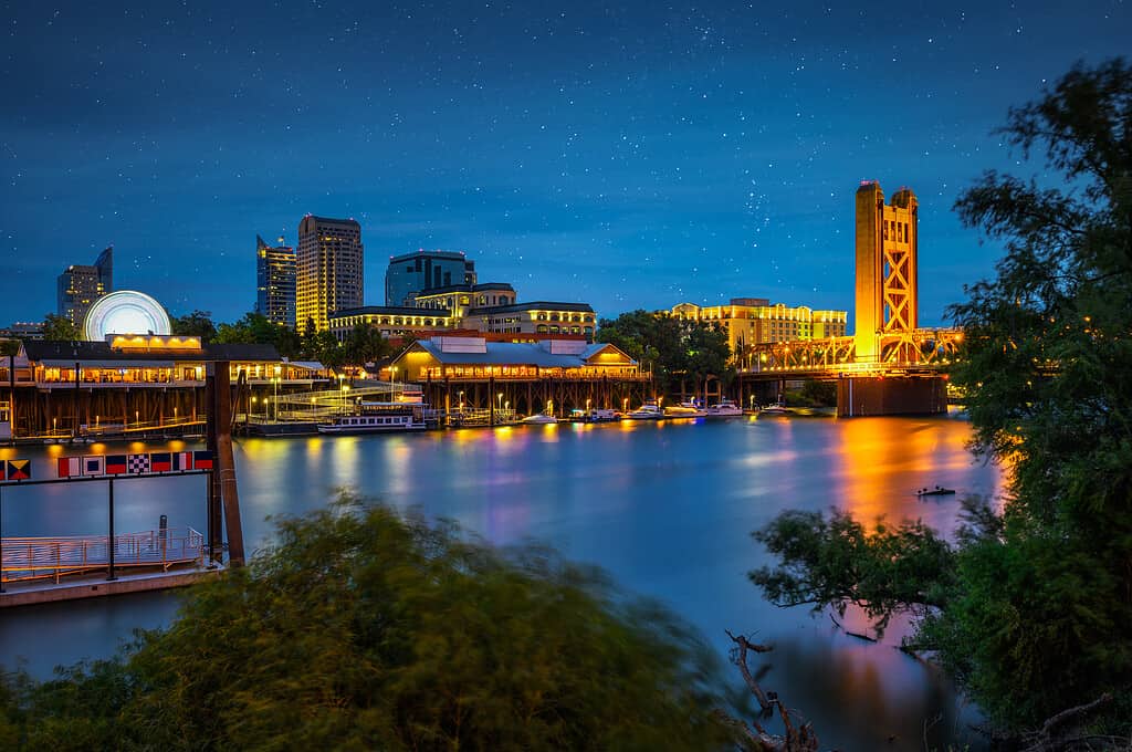 Gold Tower Bridge and Sacramento River in Sacramento, California, photographed from River Walk Park at night with stars in the sky.