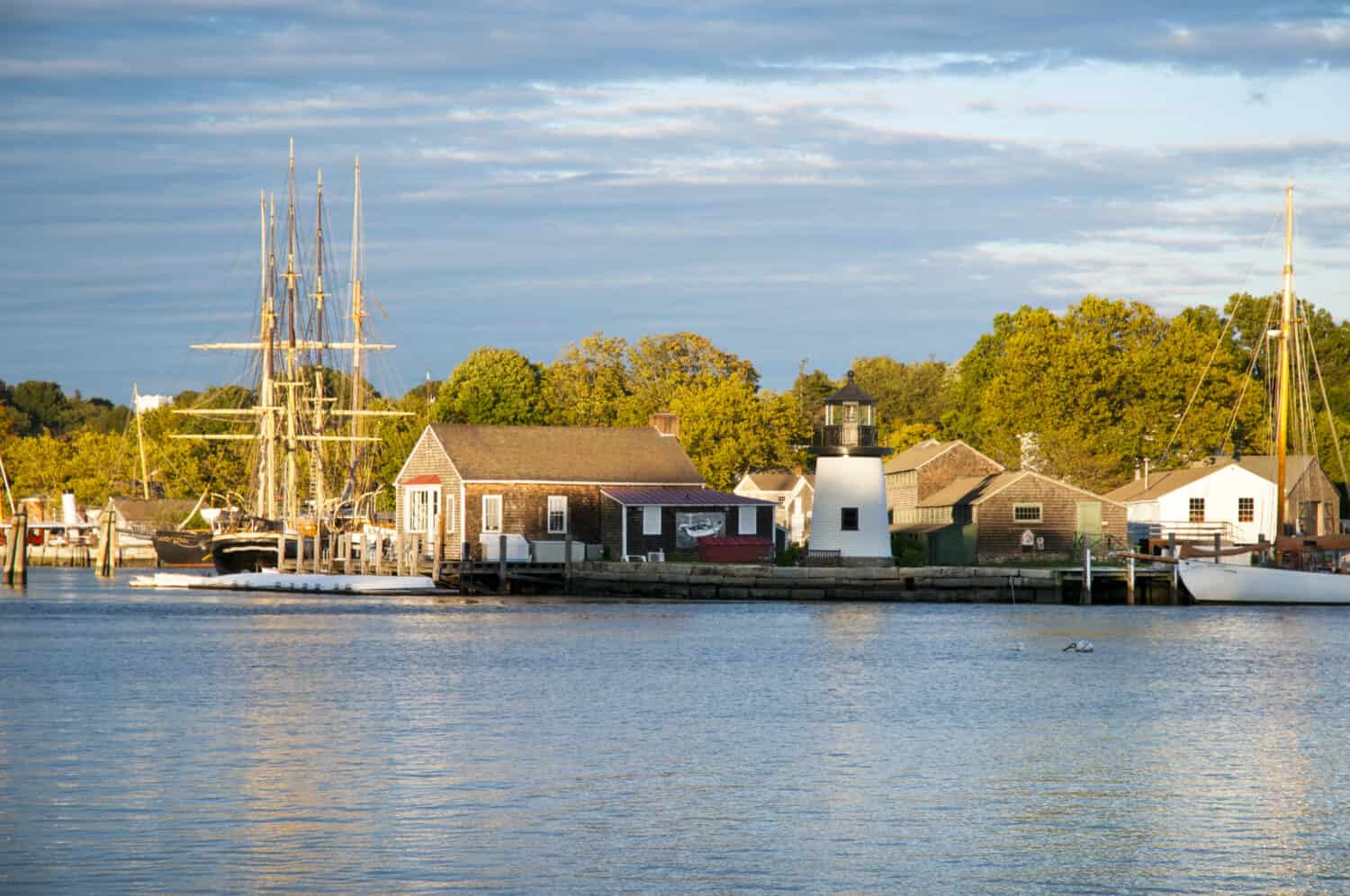 Sun setting in front of Mystic Seaport, an outdoor recreated 19th century seaport in Connecticut. Visitors will find a whaling ship, and replica of Brant Point light from Nantucket Island.