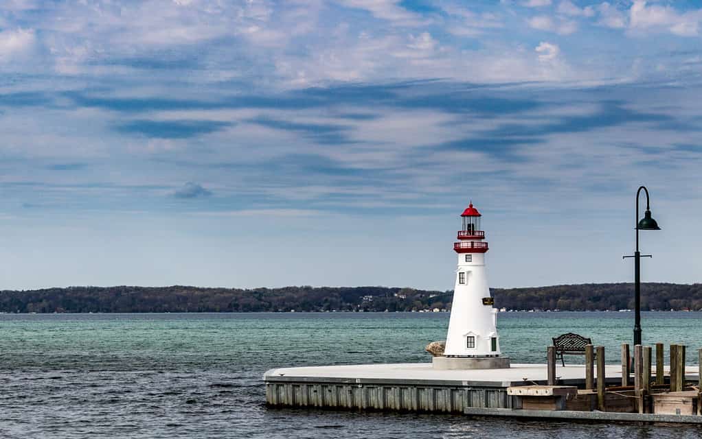 Torch Lake Lighthouse at the end of a pier.  Blue water and skies.