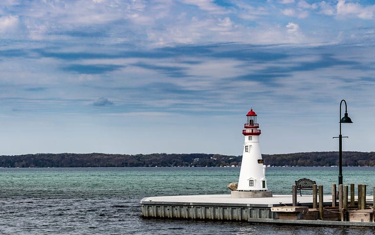 Torch Lake Lighthouse at the end of a pier. Blue water and skies.