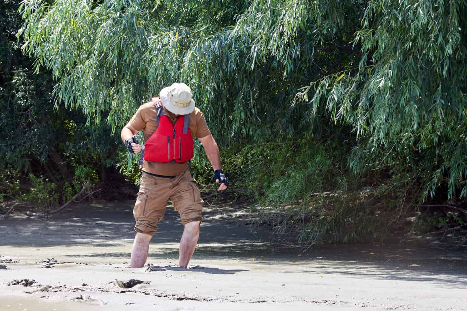 Man standing in natural quicksand river, clay sediments, sinking, drowning quick sand, stuck in the soil
