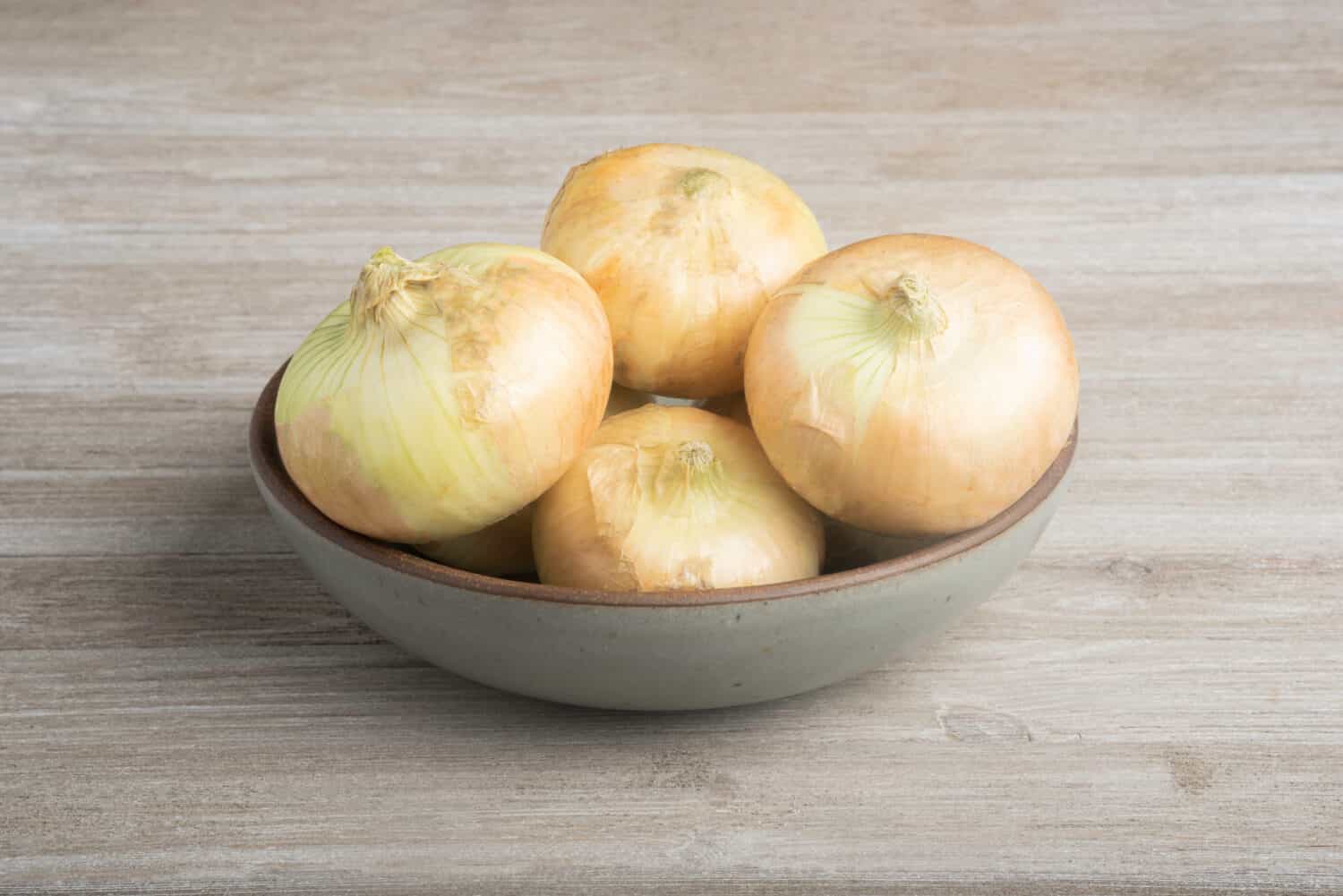 A bunch of authentic southern sweet white onions artfully arranged on a ceramic bowl placed on a white painted rustic wood panel board.