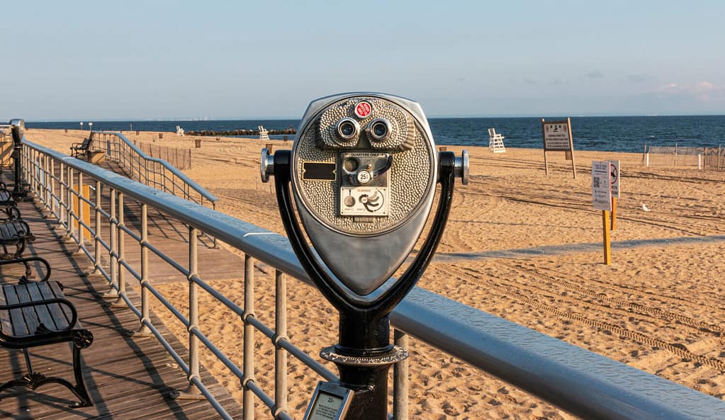 A coin operated binoculars on the boardwalk at Sunken Meadow State Park overlooking a beach toward Connecticut over the Long Island Sound.