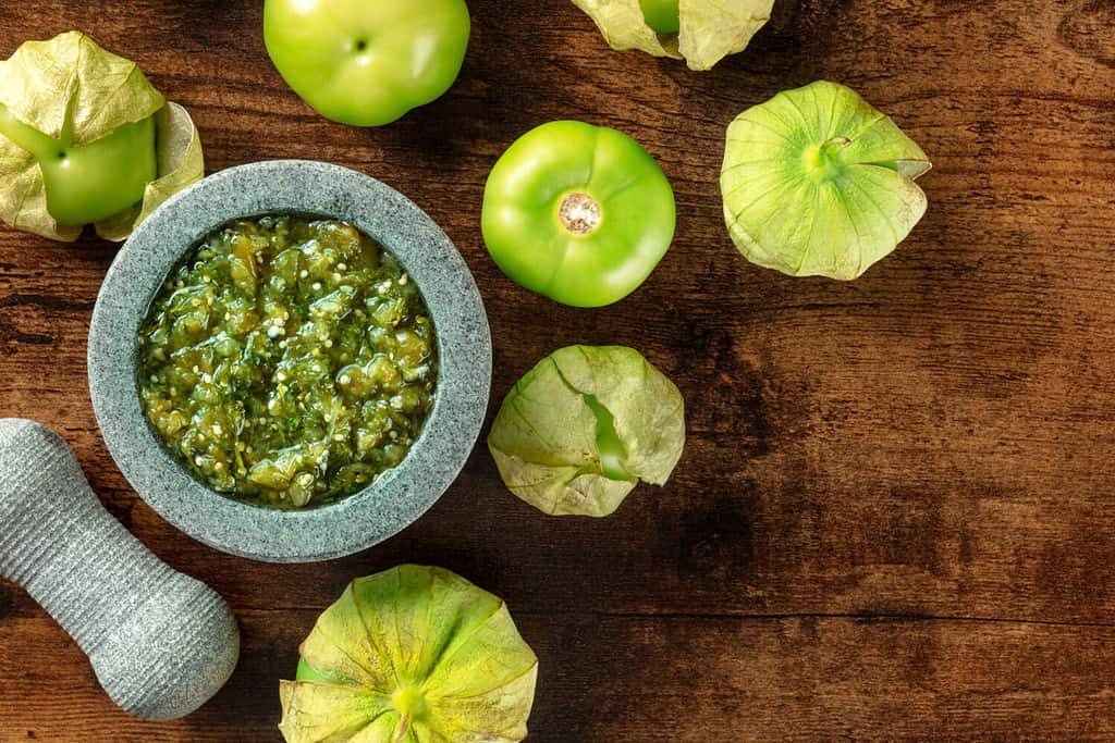 Tomatillos, green tomatoes, with salsa verde, green sauce, in a molcajete, traditional Mexican mortar, overhead flat lay shot with a place for text
