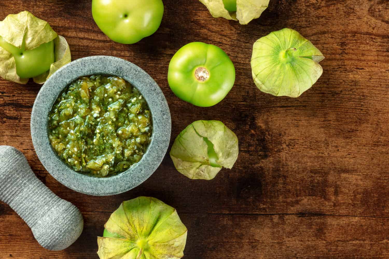 Tomatillos, green tomatoes, with salsa verde, green sauce, in a molcajete, traditional Mexican mortar, overhead flat lay shot with a place for text