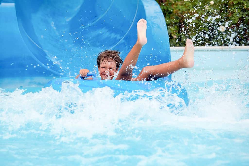 happy an 8 year old boy is riding in the water Park on inflatable circles on water slides with splash