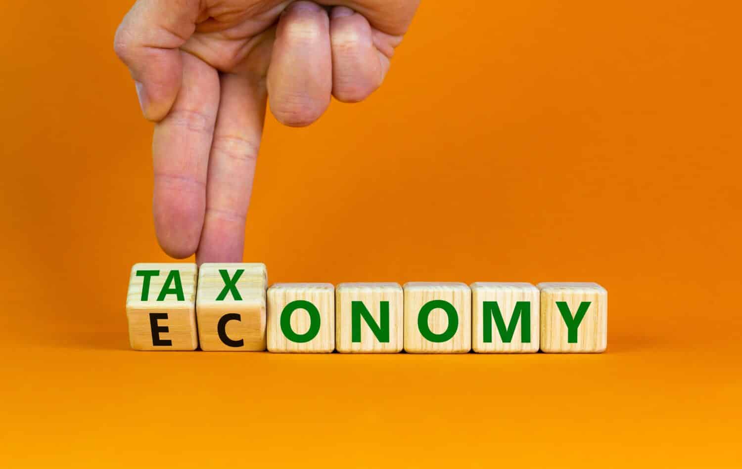 Taxonomy or economy symbol. Businessman turns cubes, changes the word economy to taxonomy. Beautiful orange table, orange background, copy space. Business, ecology and taxonomy or economy concept.