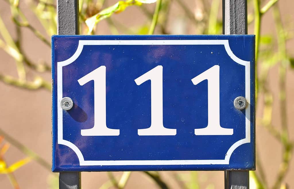 A blue house number plaque, showing the number hundred and eleven (111)
