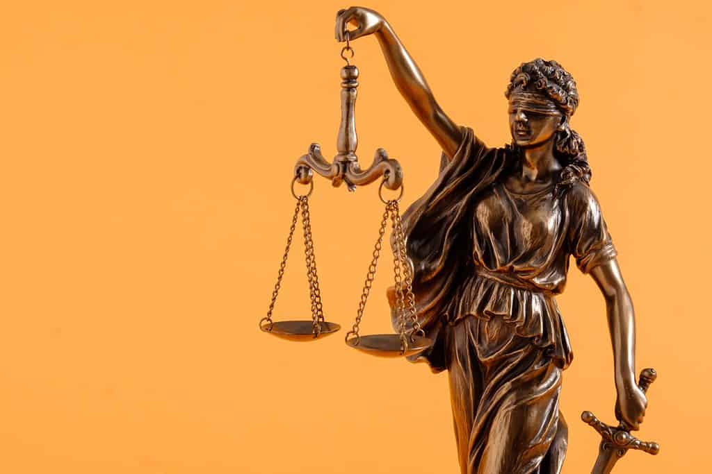 Brass figure of justice holding scales over a bright orange background with copy space