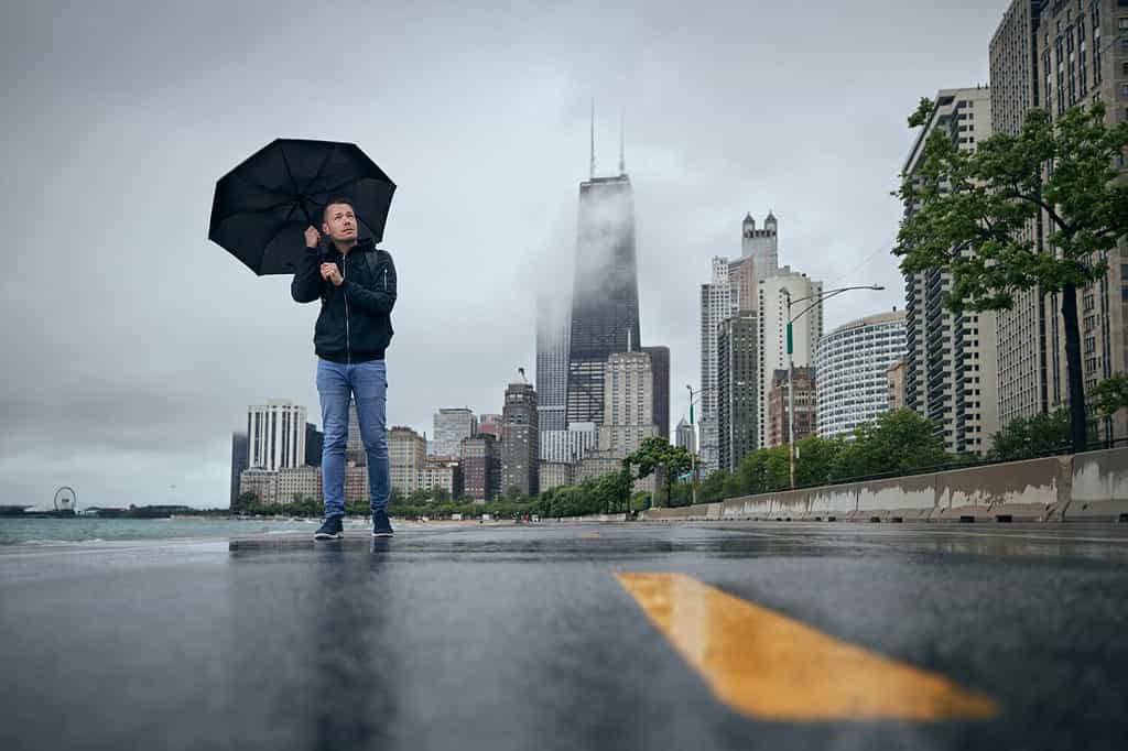Man with umbrella walking against Chicago cityscape. Rainy and windy day in city.