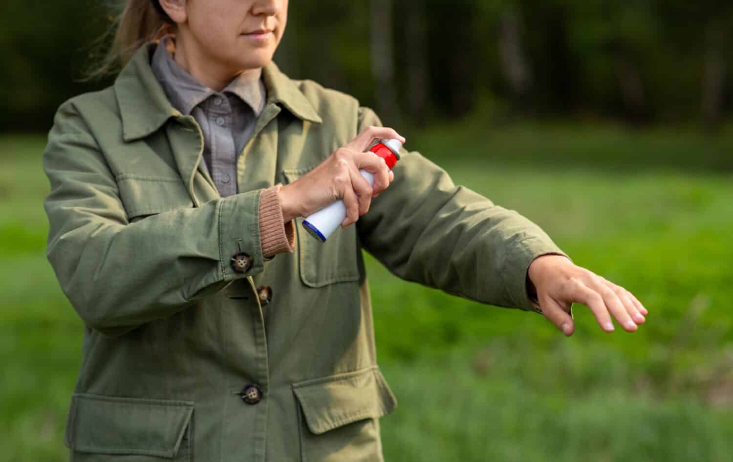 health care, protection and people concept - woman spraying insect repellent or bug spray to her hand at park