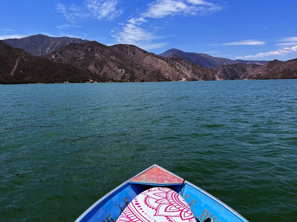 First person vies of fishing boat cruising on pyramid lake in California, USA. Ego perspective of blue boat floating on green water of mountain lake during summer in San Bernadino Mountains.