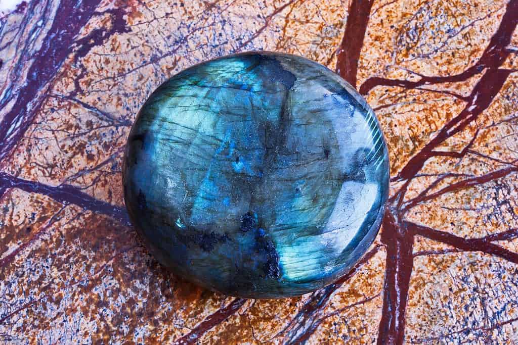 Close-up of natural gemstone polished blue-green labradorite mineral on brown polished marble slab.