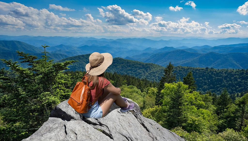 Hiker girl sitting on a cliff edge enjoying scenic summer view. Woman relaxing on top of autumn mountain, over the clouds. Blue Ridge Parkway ,near Asheville, North Carolina, USA.