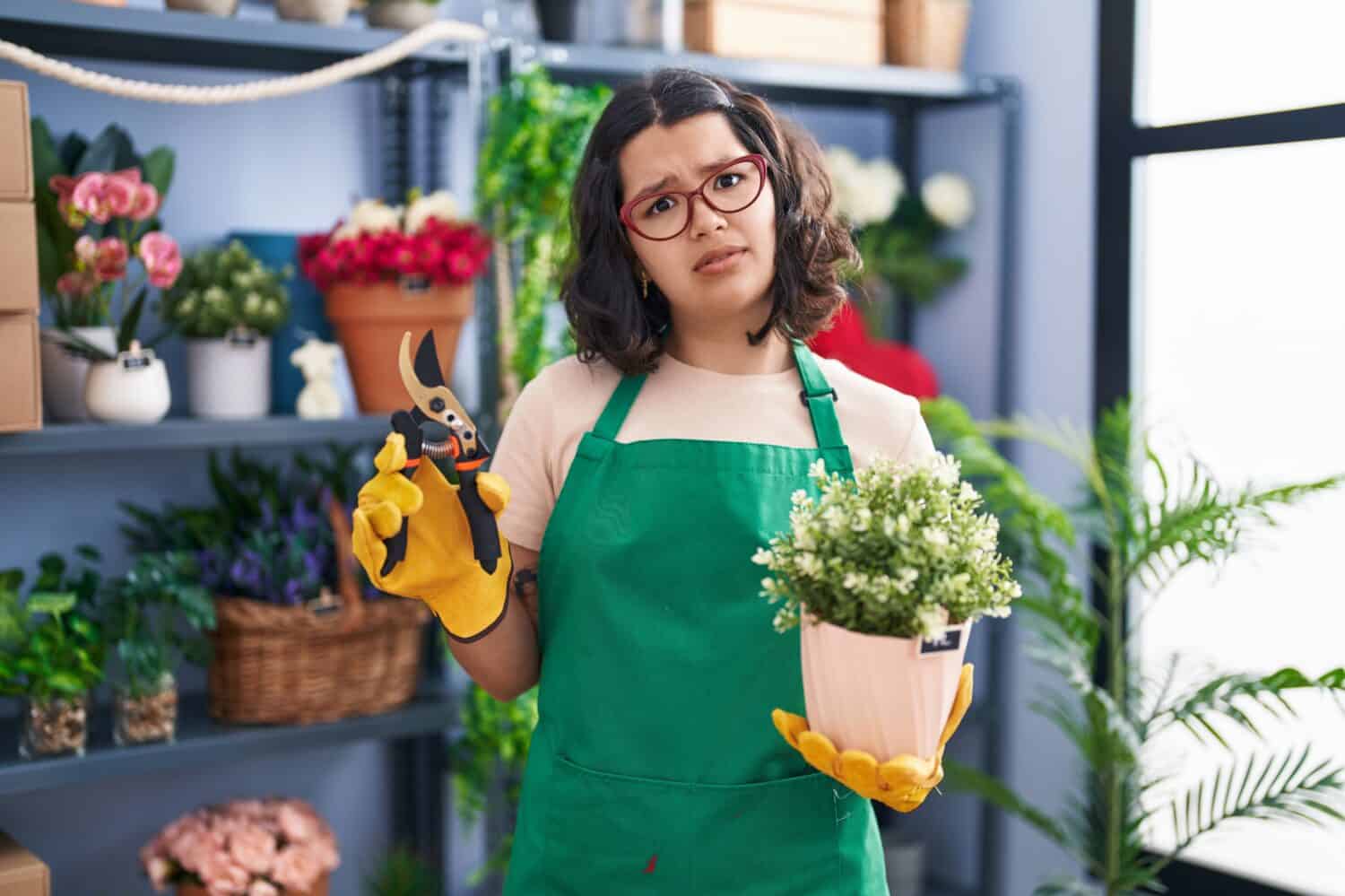 Young hispanic woman holding a plant with a  confused expression. 