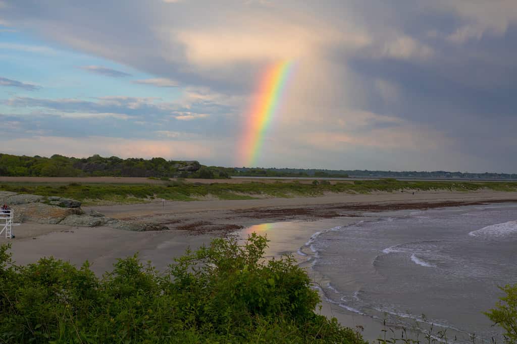 A natural occurring rainbow over Sachuest's Beach (Second Beach) in Newport, Rhode Island after an early summer rain storm Shot June, 2017. Rainbow over water and sand.