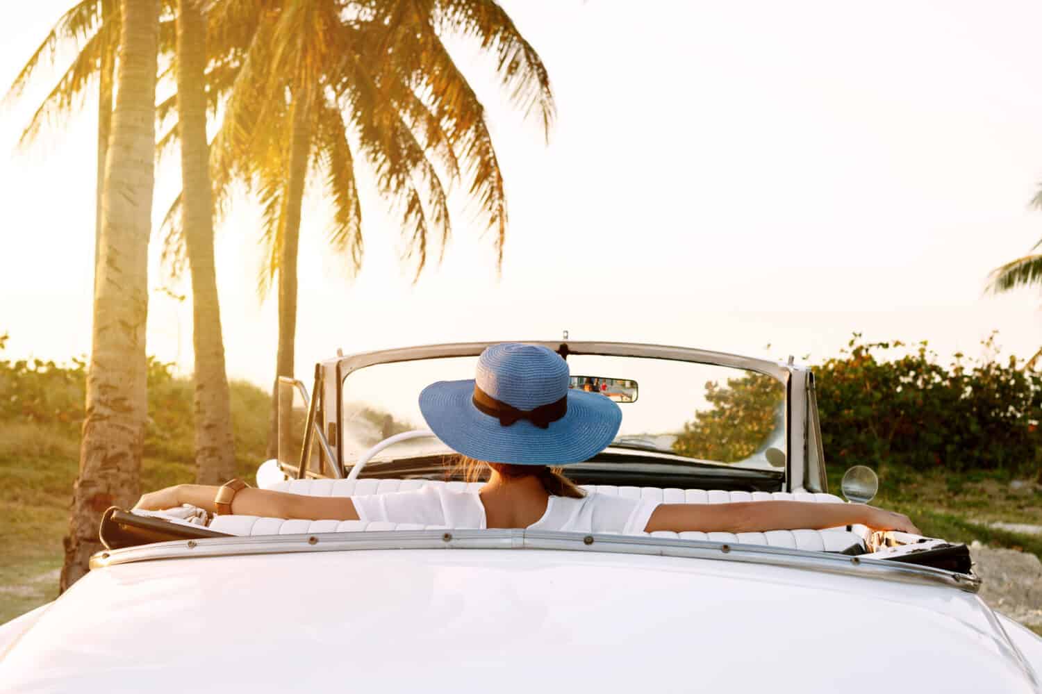 Beautiful woman in blue hat and white retro cabriolet on the beach