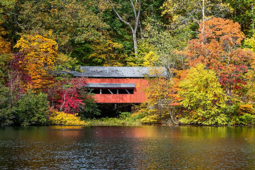 With beautiful reflections on Lake Loretta in Alley Park, Lancaster, Ohio, the red George Hutchins Covered Bridge, surrounded by colorful autumn leaves, was constructed in 1865 at another location.