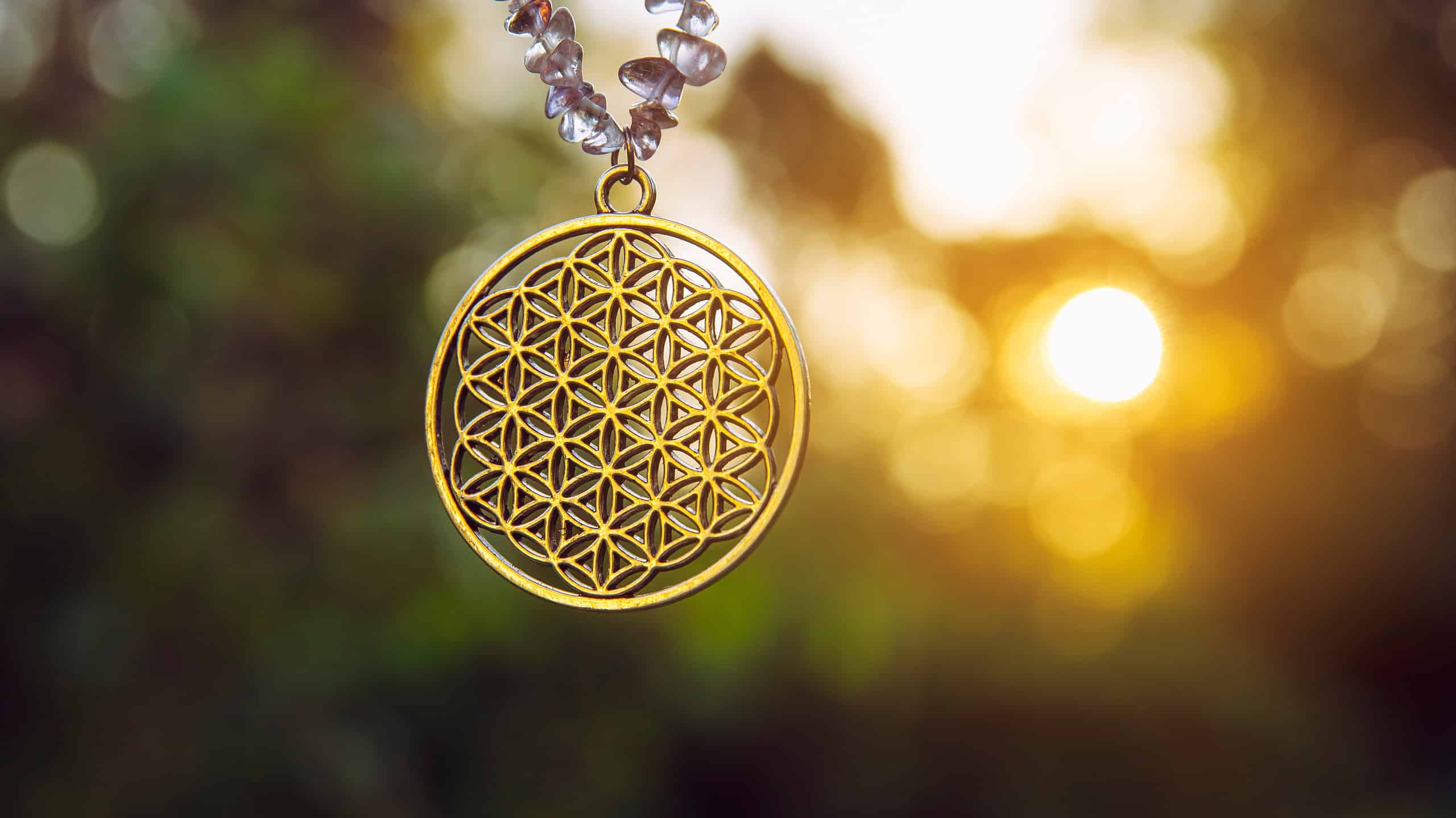 Flower of Life symbol pendant amulet with sun shining though hanging outdoors with lot of copy space. Good luck charm.