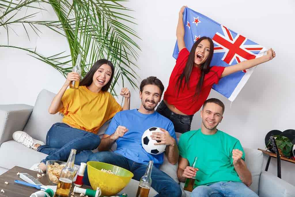 Group of friends sport fans watching match in colorful shirts girl holding new zealand flag