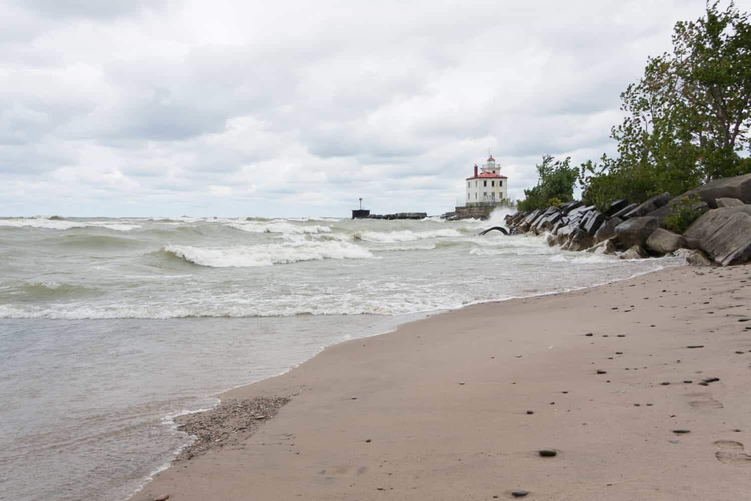 Lighthouse at Mentor Headlands Beach State Park in Ohio with waves crashing on shore and dark clouds overhead. 