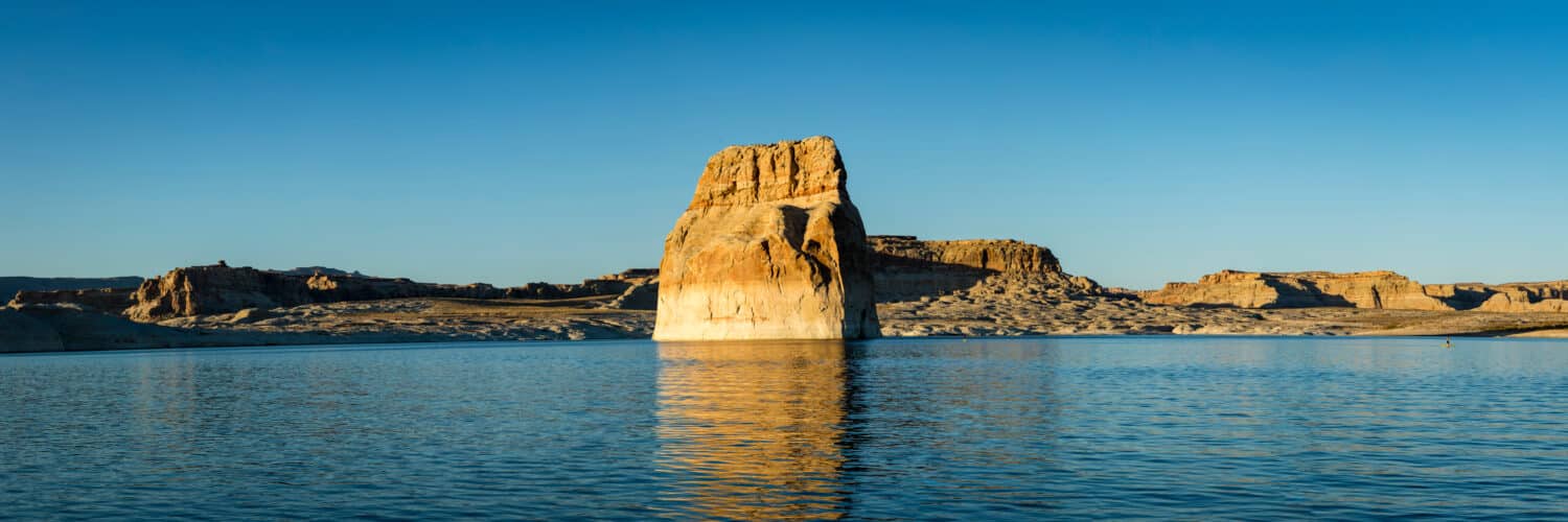 lone rock in lake powell near sunset on a calm evening with serene blue waters