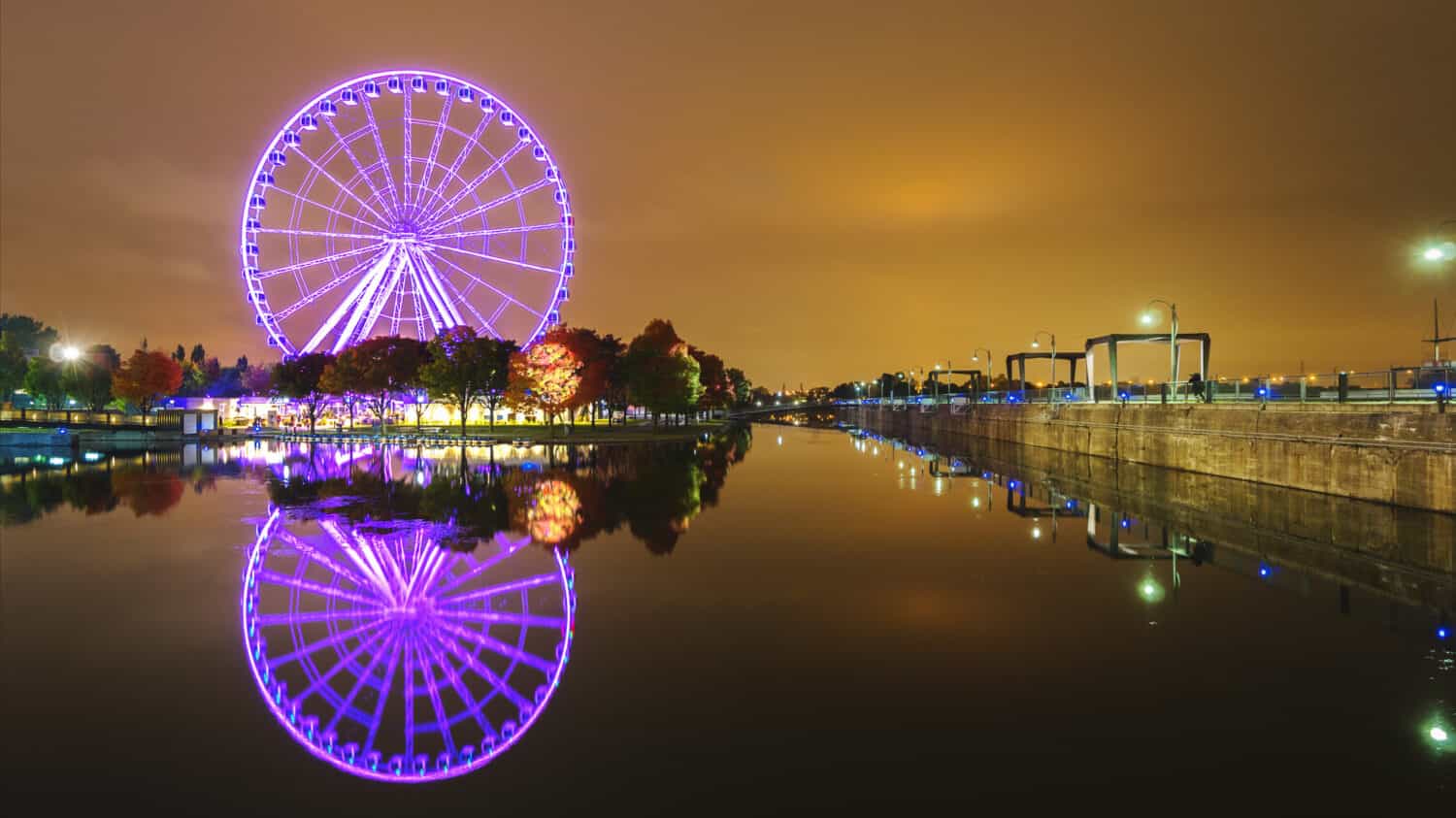 A large Ferris wheel in Montreal is effectively reflected in the water. Night city
