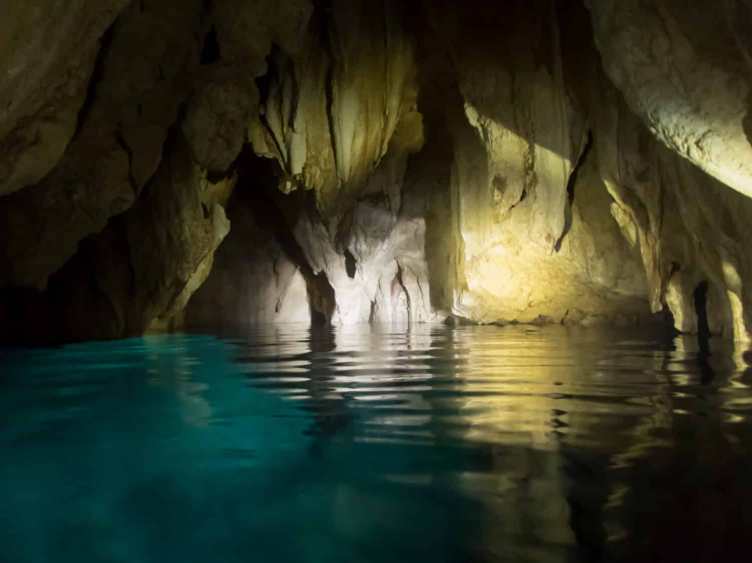 Chandelier cave underneath Rock Islands in Pacific with glowing turquoise colored water and stalactites.