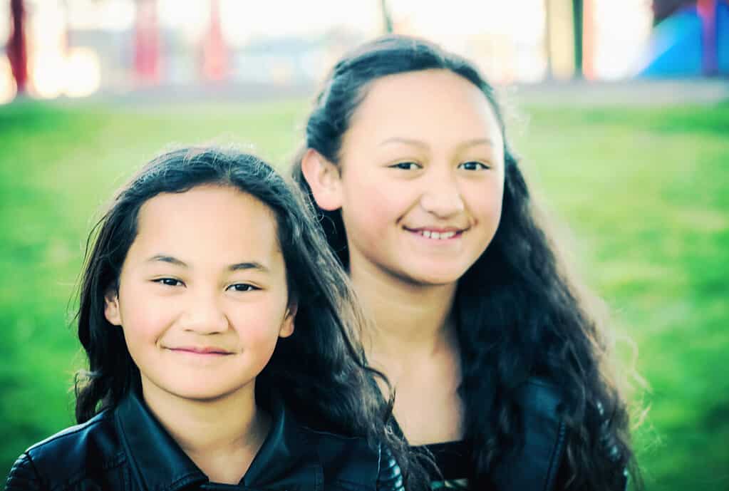 Portrait of two young Maori sisters taken outdoors in a park.