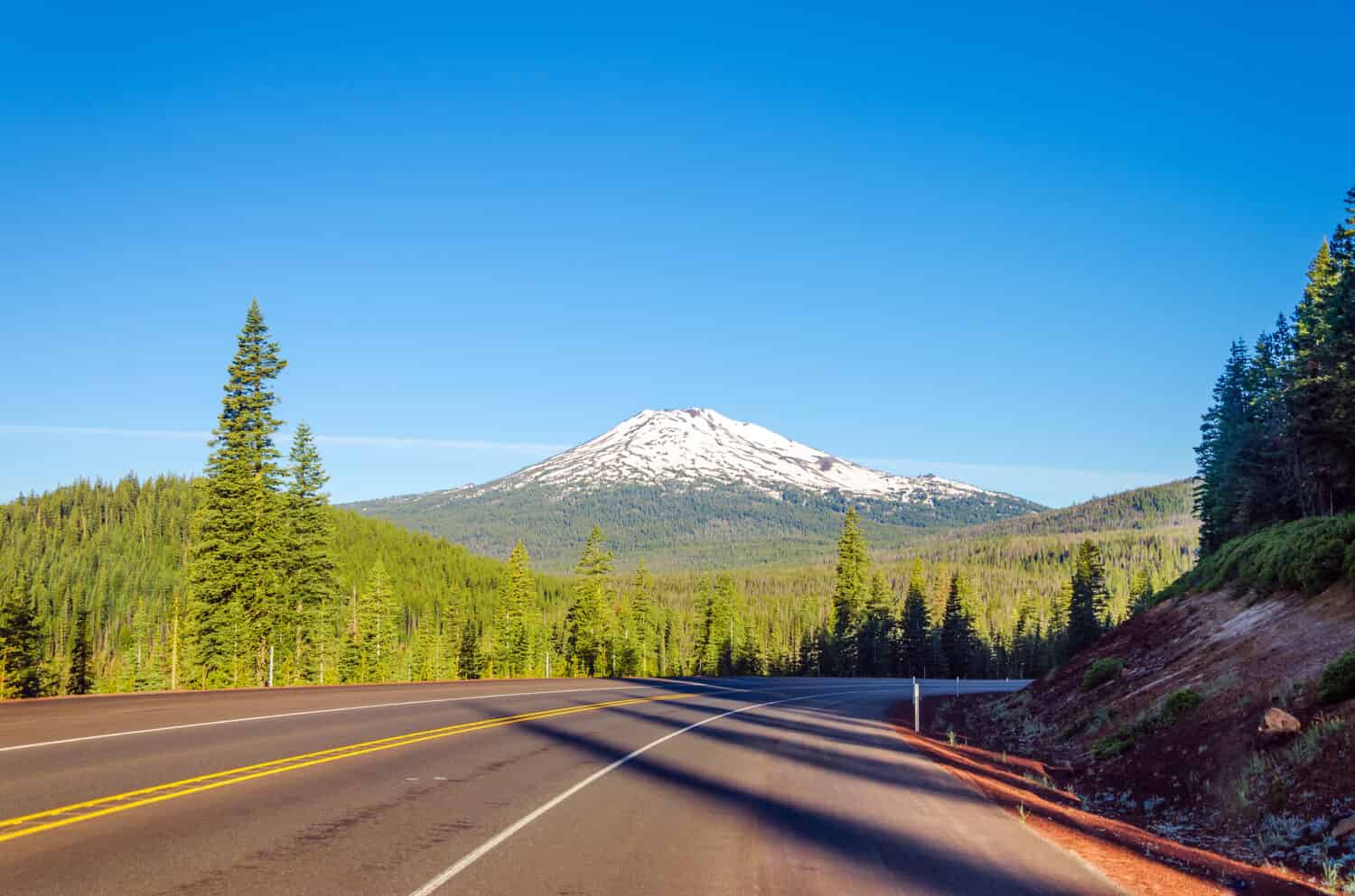 Curving highway with a dramatic view of Mt. Bachelor and beautiful green pine tree forest near Bend, Oregon