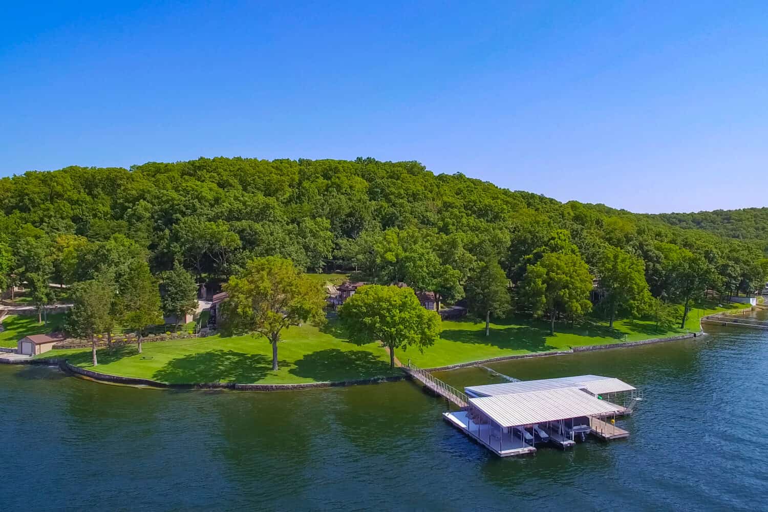 Lakeside home and dock at Lake of the Ozarks Missouri on a summer sunny day with green trees, blue water, and blue sky.