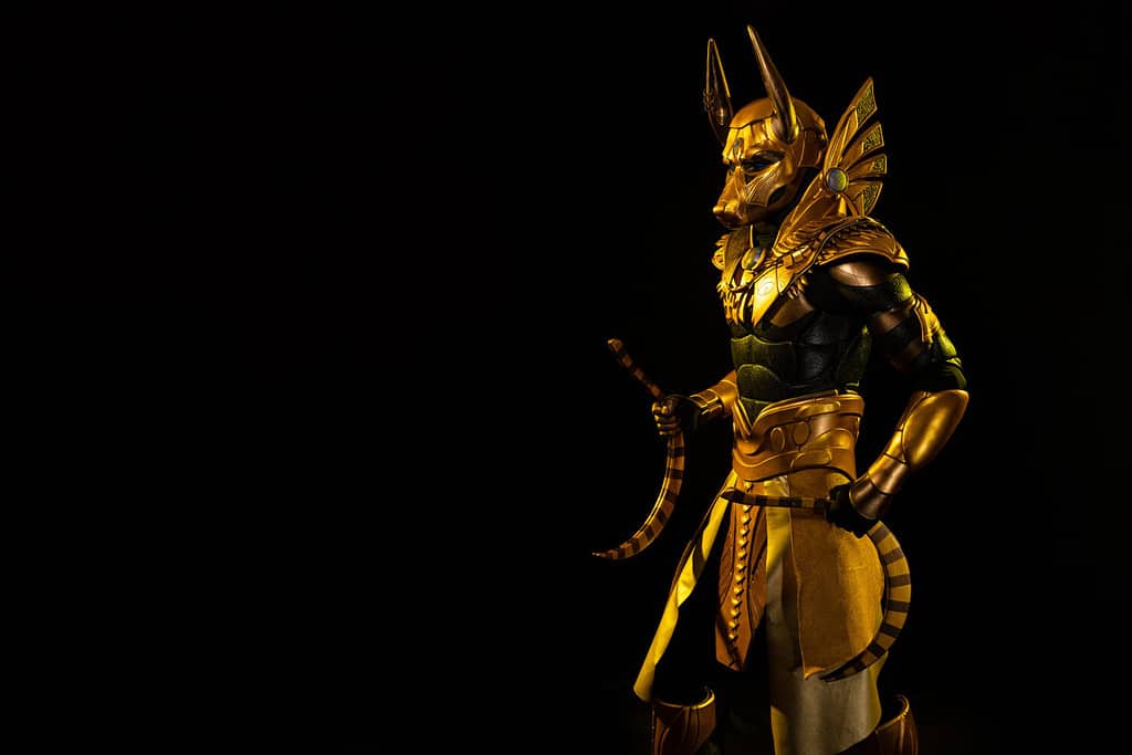 a male actor in a suit of an Egyptian mythology character, the golden deity Jackal Anubis, twists buugeng in yellow light on a black background