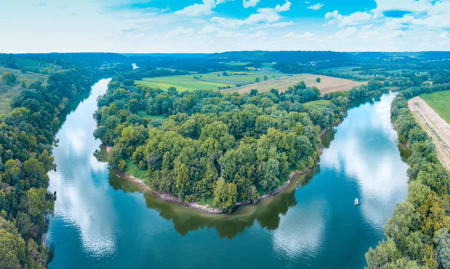 An aerial view panorama of lush forestry and bending Kentucky river with a boat on the water and cloud reflections in the sky.