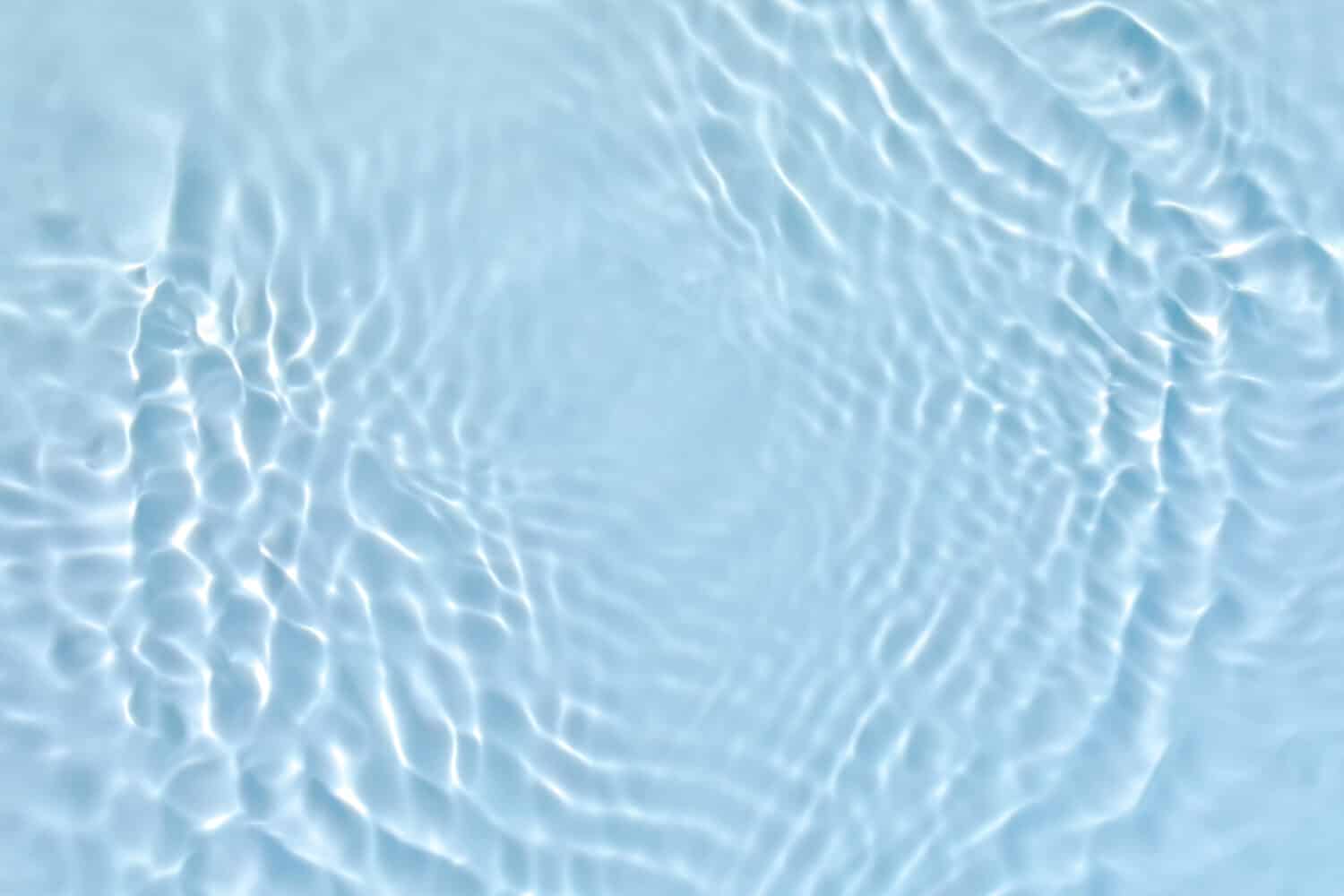 Blurred transparent blue colored clear calm water surface texture with splashes and bubbles. Trendy abstract nature background. Water waves in sunlight.
