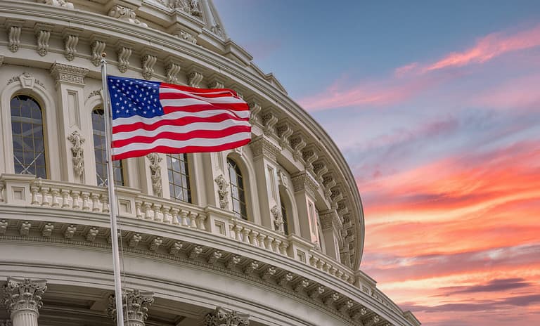 View of the United States Capitol Rotunda Dome in Washington DC with the Star Spangled American Flag against colorful dramatic sunset sky background