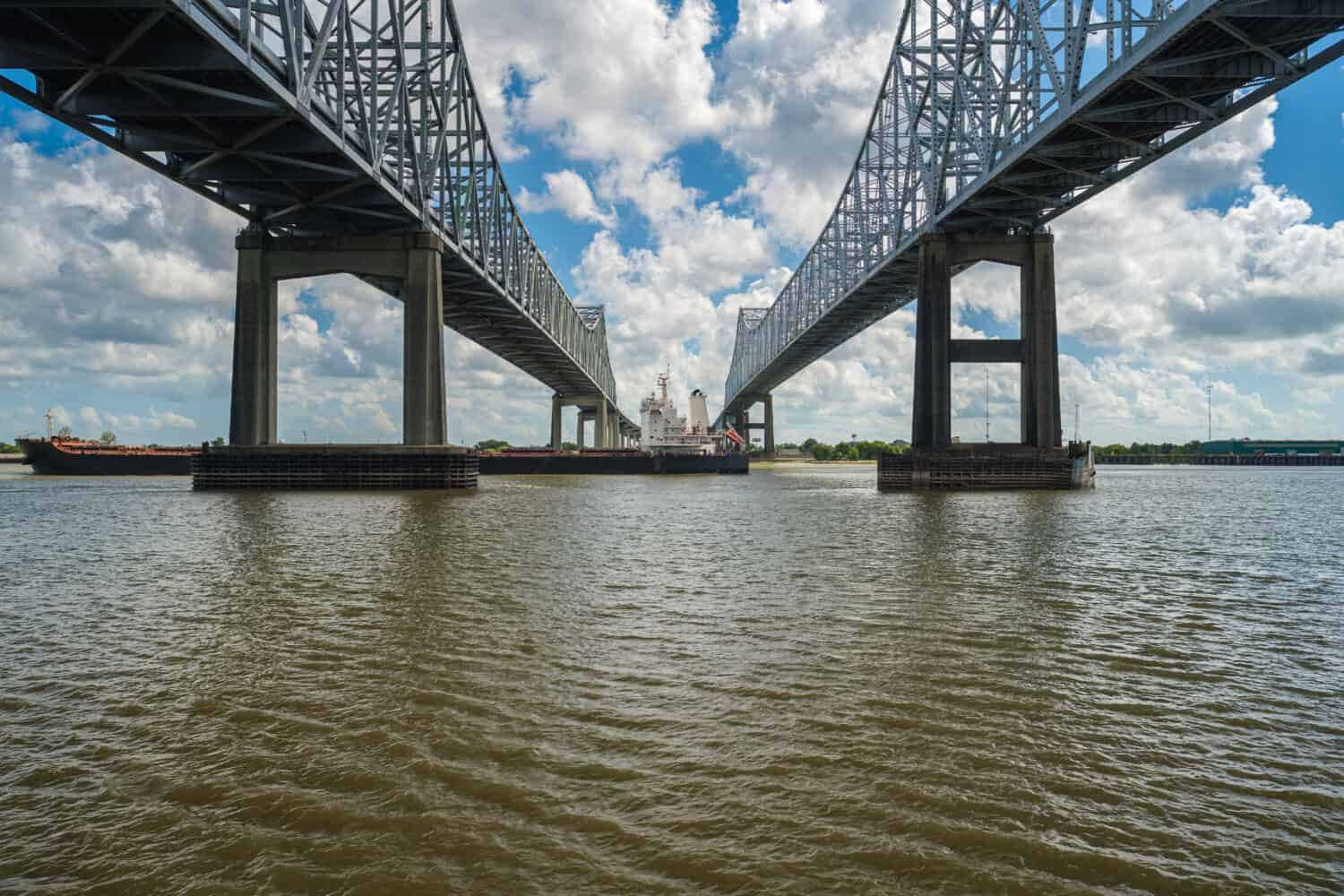 interstate 10 bridge over the Mississippi River in New Orleans, Louisiana with a cargo ship cruising by.
