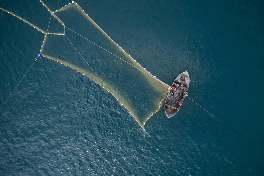 Vintage wooden boat in coral sea. Boat drone photo. A fisherman on a fishing boat is casting a net for catching fish.