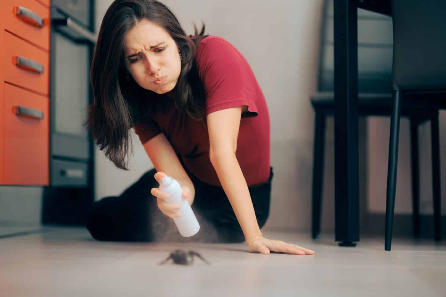 Woman Spraying with Insecticide Over an Ant on the Kitchen Floor. Homeowner dealing with pest infestation problem in her own apparent
