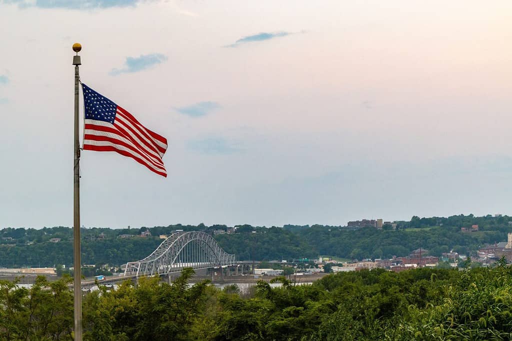 A view of the American flag and Julien Dubuque Bridge against blue sky at sunset in Dubuque city, Iowa, United States