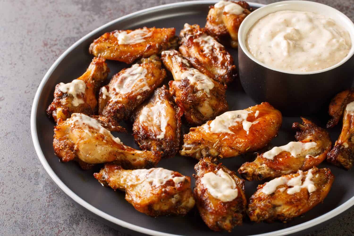 A plate of hot wings with some white sauce on the side. 