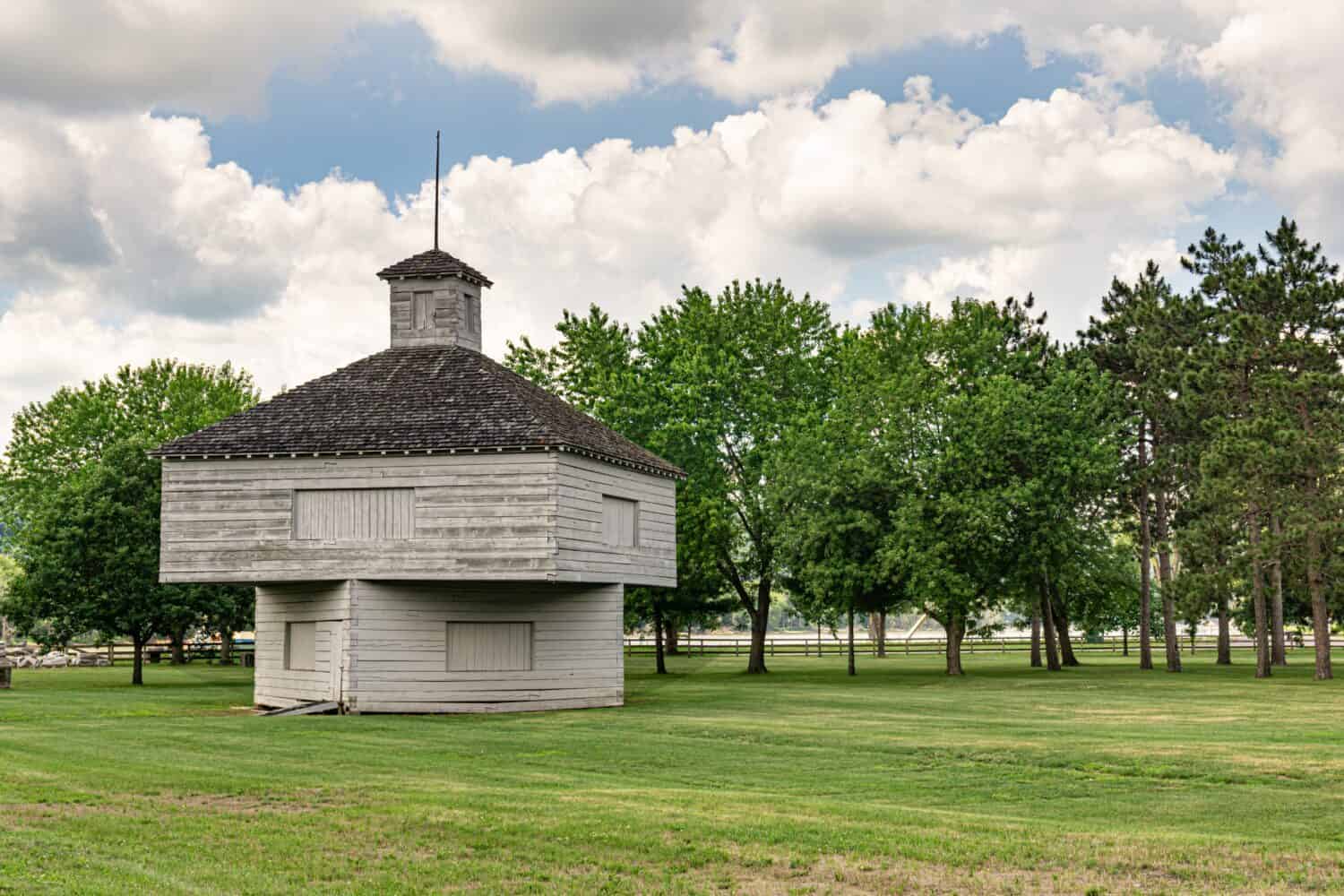 Old Fort Crawford building on St. Feriole Island sits in a green grass park, surrounded by trees, and backed by the Mississippi River in Prairie du Chien, Wisconsin.